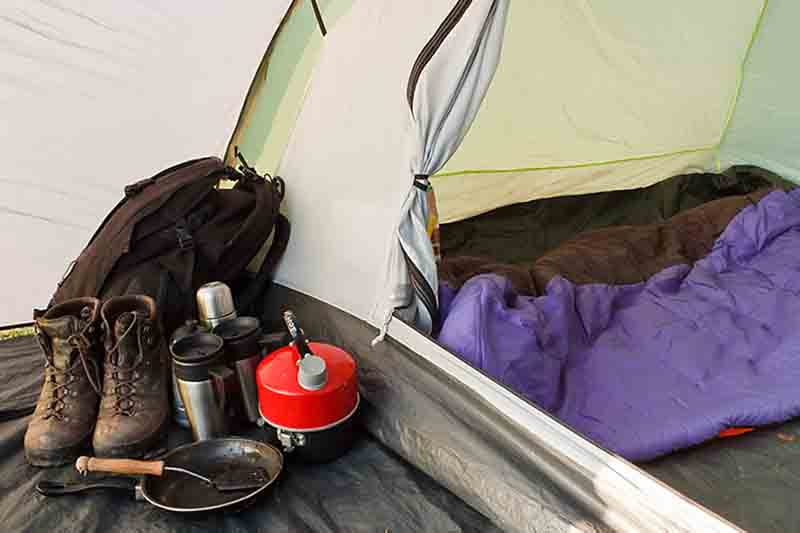 Interior view of a tent set up with various equipment and sleeping bag inside inner compartment, and gear in the vestibule, showing a well organized camp for camping sleeping tips
