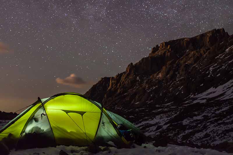Glowing tent set up on Kilimanjaro at 17,000ft, surrounded by snow and starlit sky, showcasing extreme camping conditions.