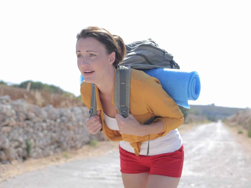 Woman hiker looking tired and weighed down by an overly packed backpack while trekking on a trail