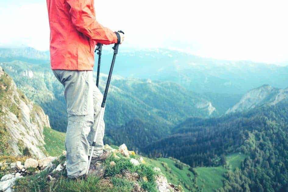 Hiker standing on a mountain ridge with trekking poles, overlooking a vast landscape