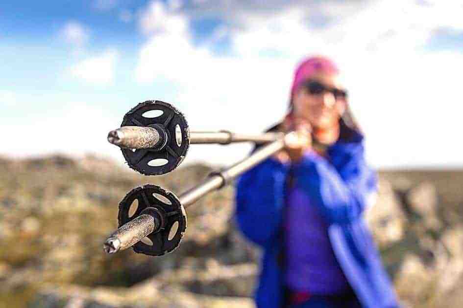 Close-up of trekking pole tips with a hiker holding them in the background