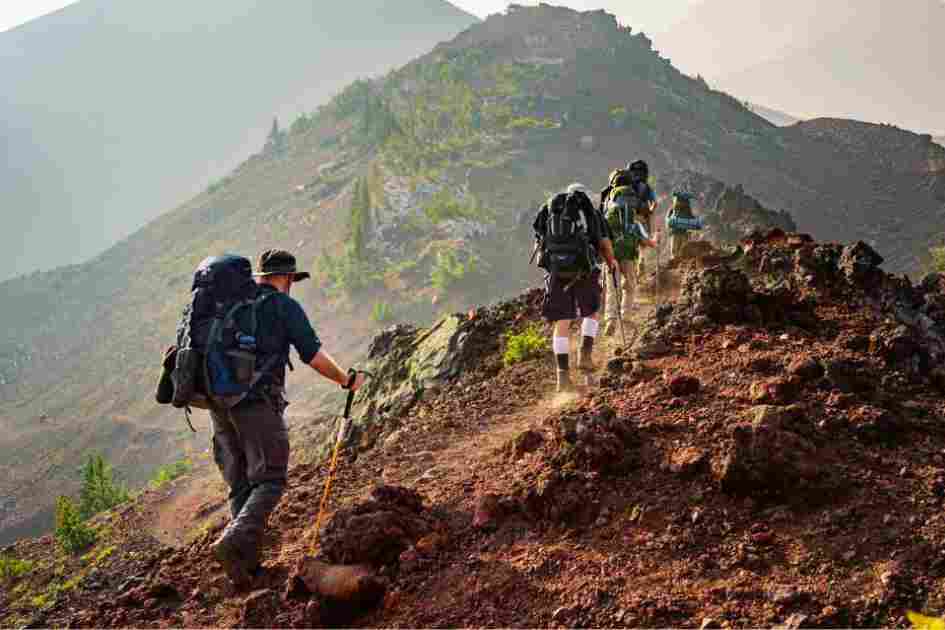 A group of backpackers hiking up a steep mountain trail, engaging leg, core, and upper body muscles.